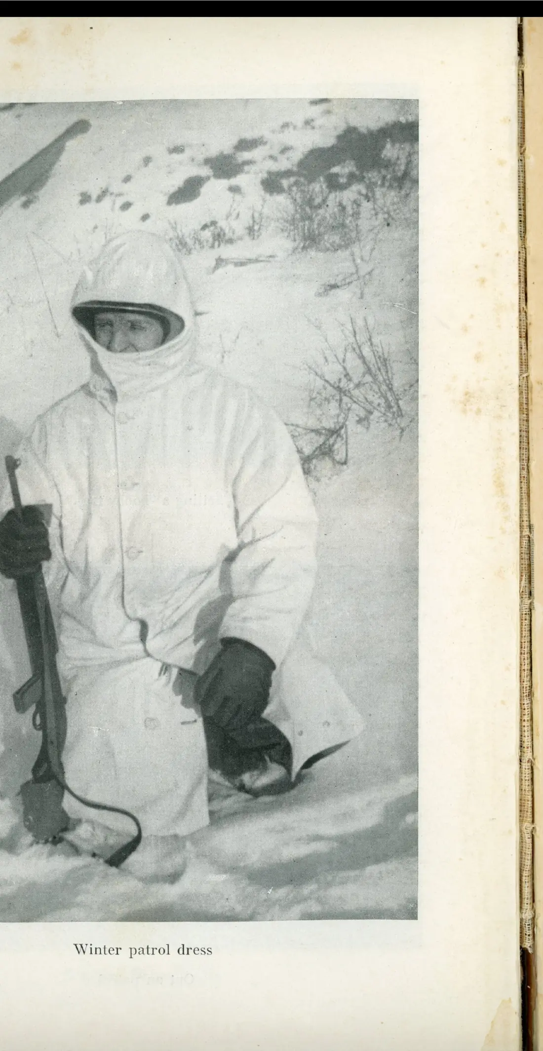 A soldier in white winter camouflage clothing, holding an entrenching tool